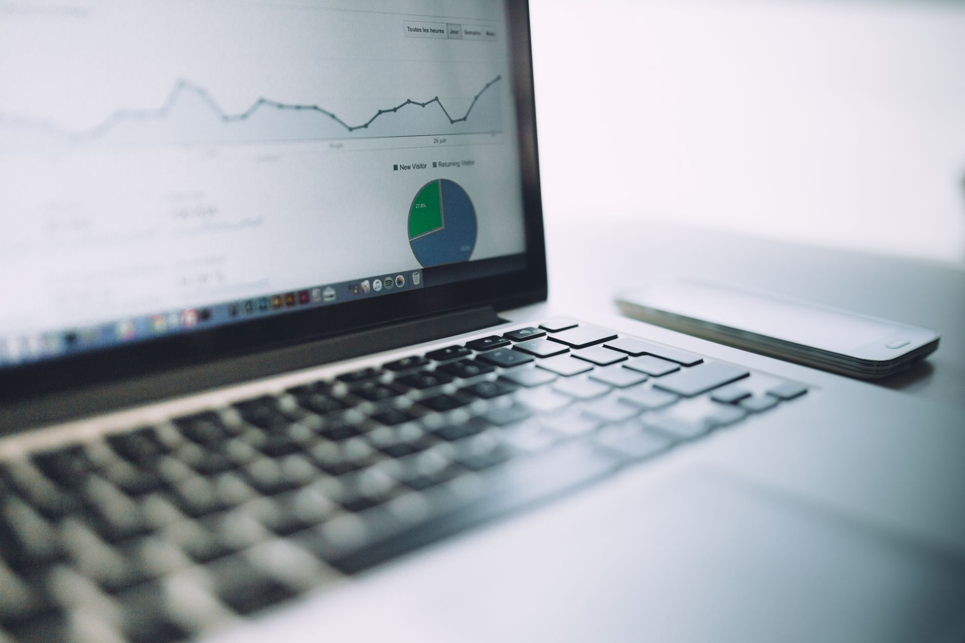Laptop displaying analytics dashboard with line graph and pie chart showing new visitor and returning visitor data