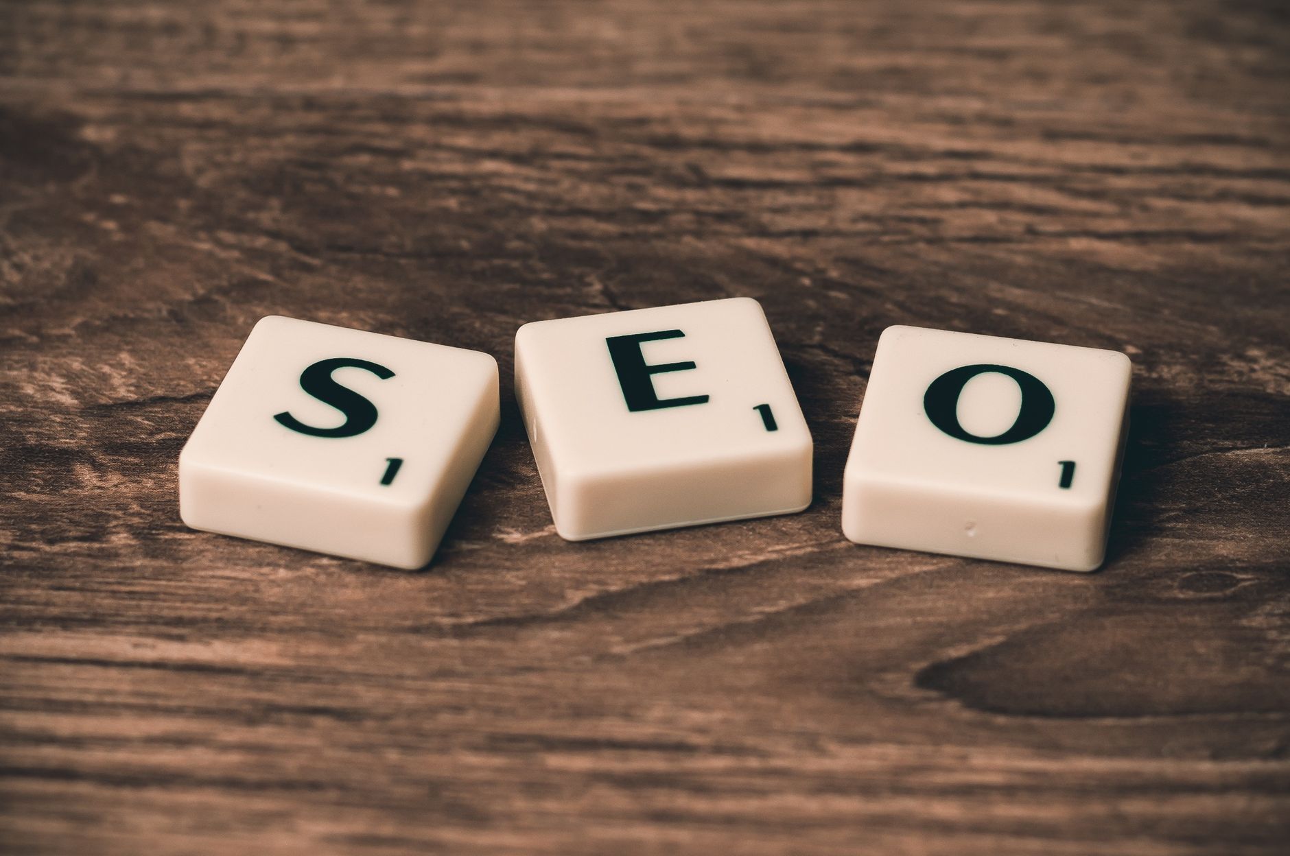 Three white Scrabble tiles spelling SEO on a dark wooden surface
