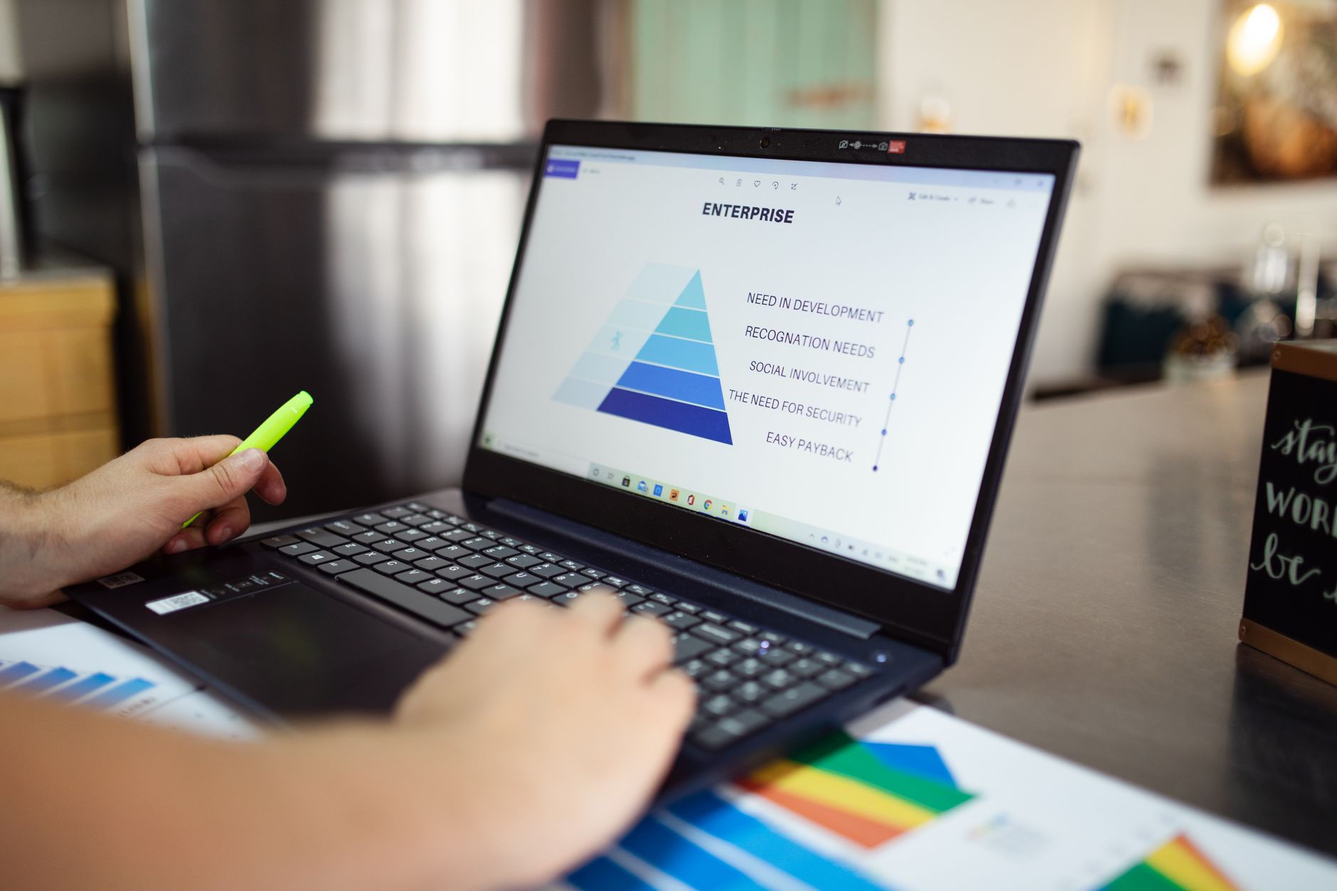 Person holding yellow pen pointing at laptop screen displaying enterprise pyramid diagram with development needs and hierarchy levels