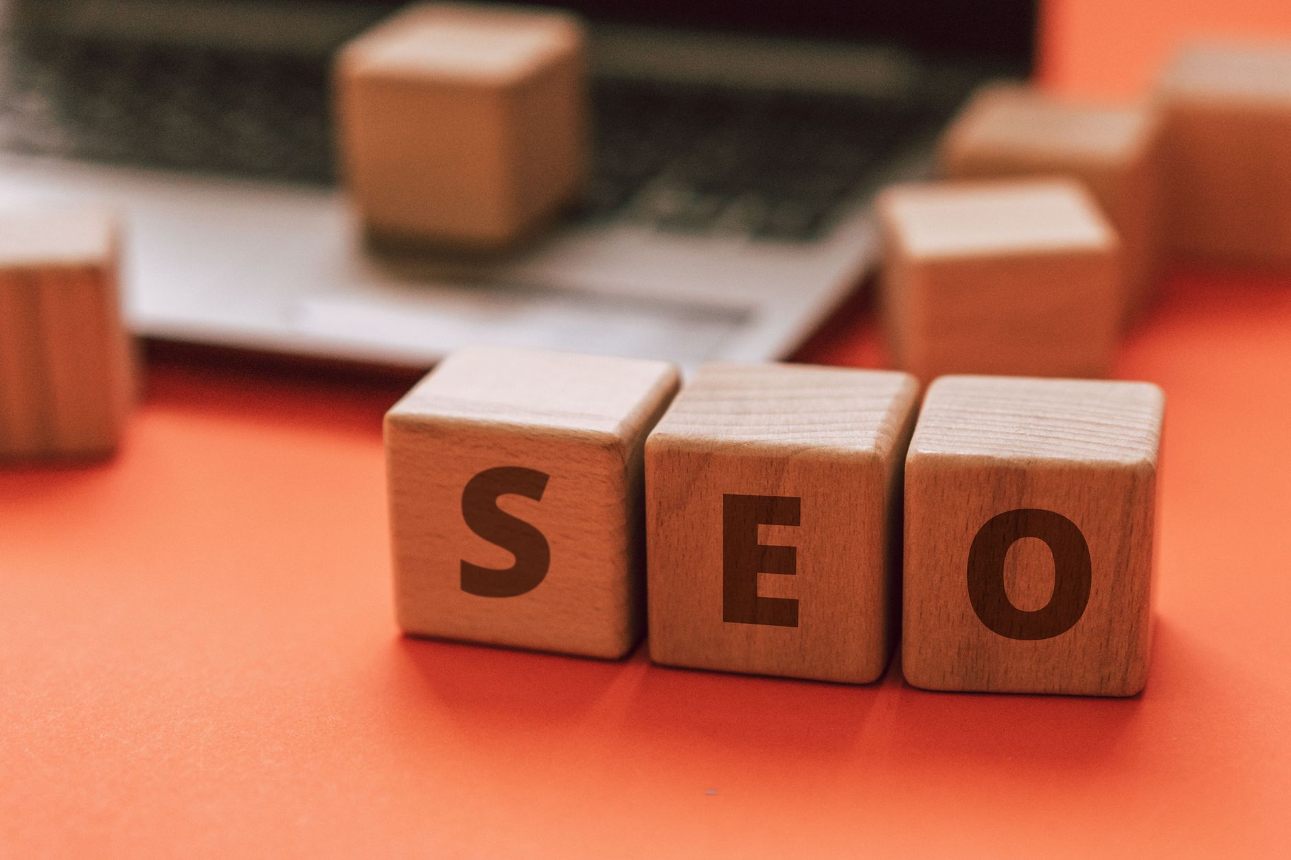 Three wooden blocks spelling SEO on an orange surface with blurred wooden blocks in the background