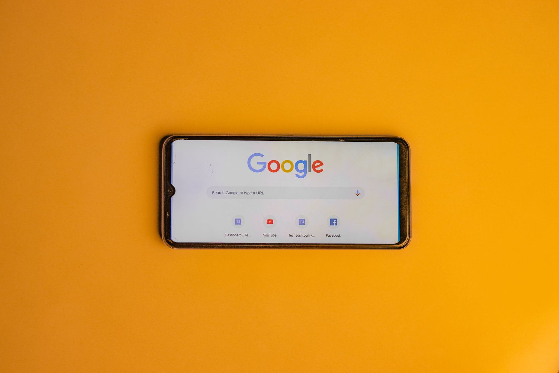 Google homepage displayed on a smartphone screen against a yellow orange background