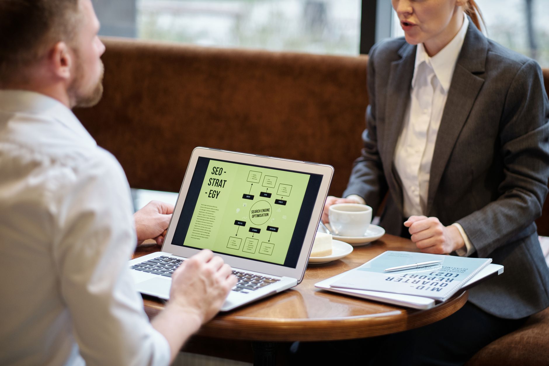 Two professionals discussing SEO strategy on a laptop displaying a flowchart diagram during a business meeting at a table with coffee cups