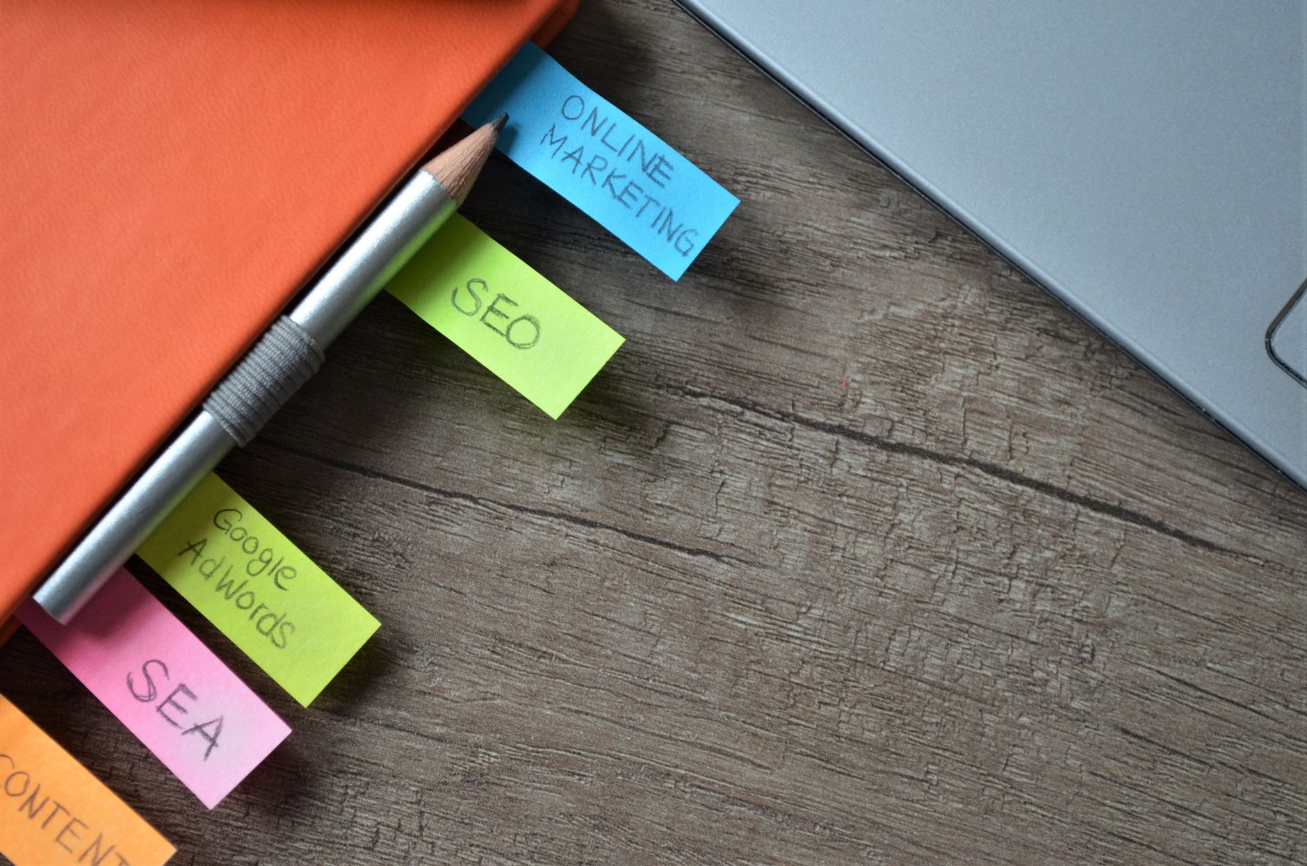 Sticky notes with marketing terms arranged on a desk next to a pencil and laptop, including SEO, Google Adwords, and Online Marketing
