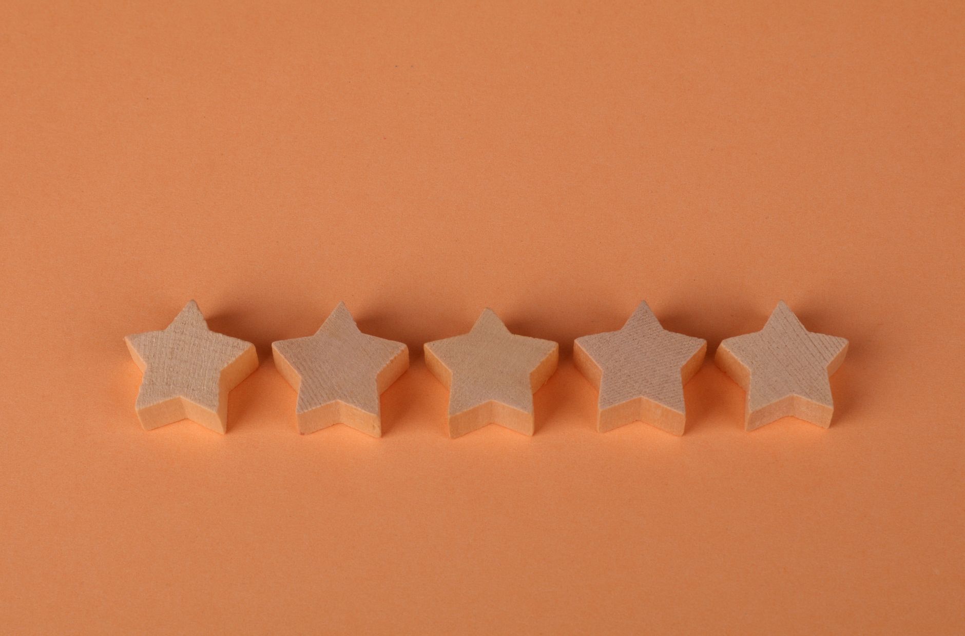 Five white wooden stars in a row on an orange background casting shadows