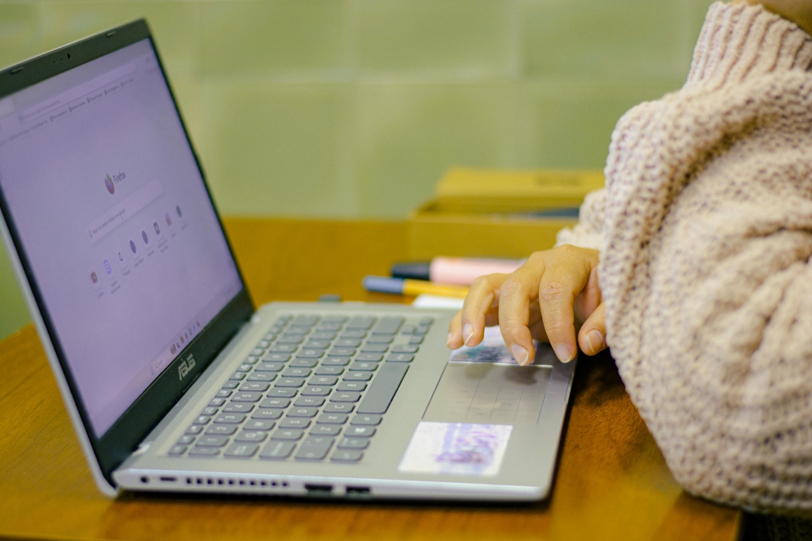 Person in cream sweater using touchpad on ASUS laptop with purple screen on yellow desk