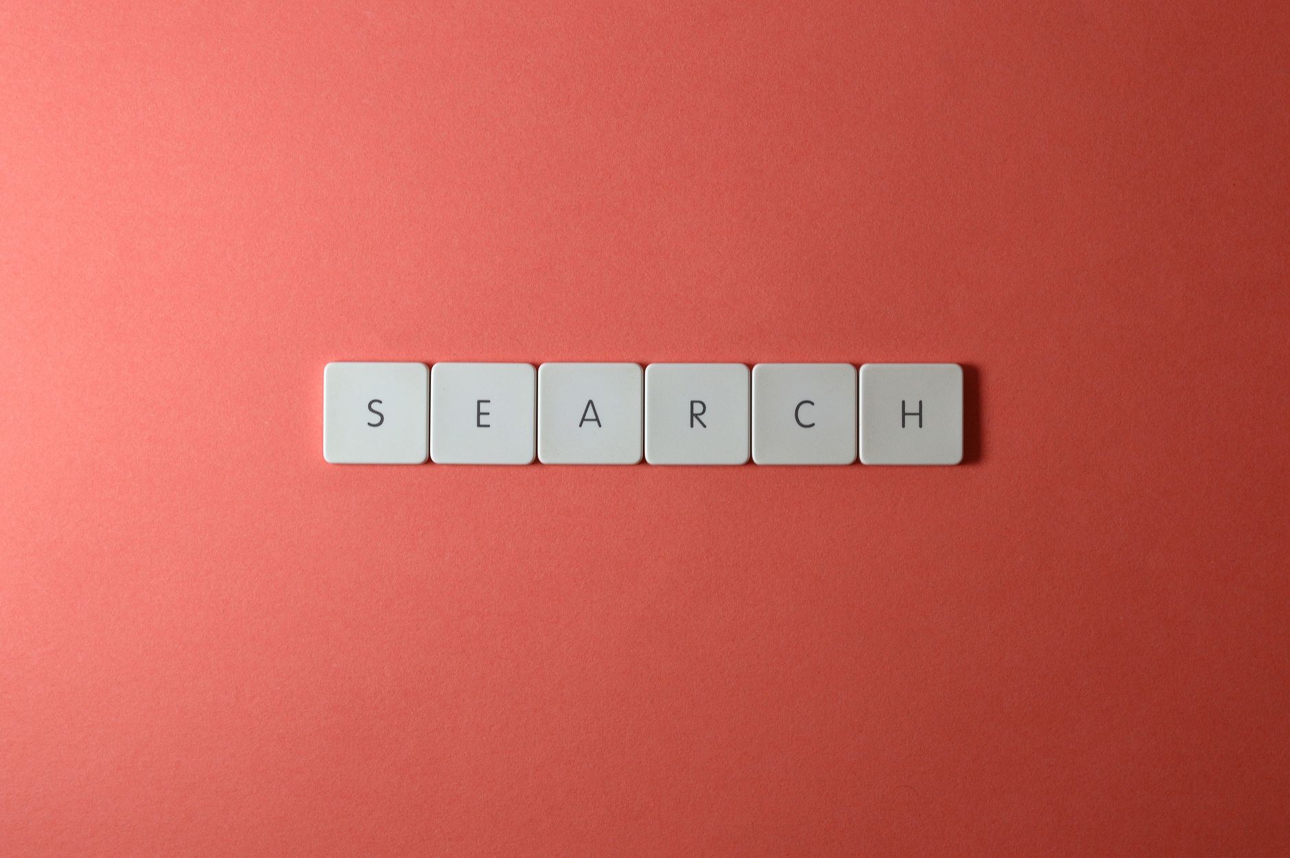 Six white letter tiles spelling SEARCH arranged horizontally on a coral red background