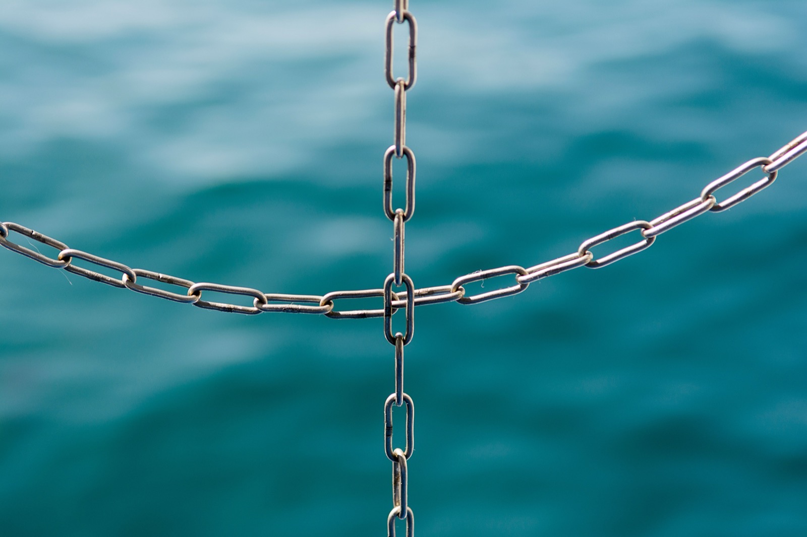 Metal chains forming a cross pattern against blurred turquoise ocean water in the background