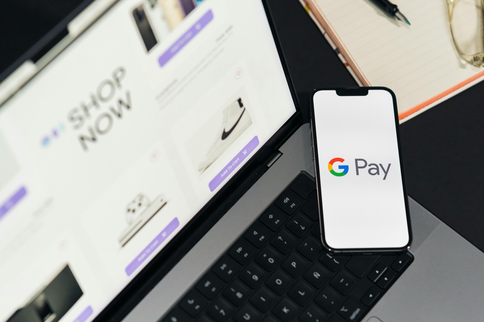 Google Pay logo displayed on smartphone screen placed on laptop keyboard with shopping website visible in background
