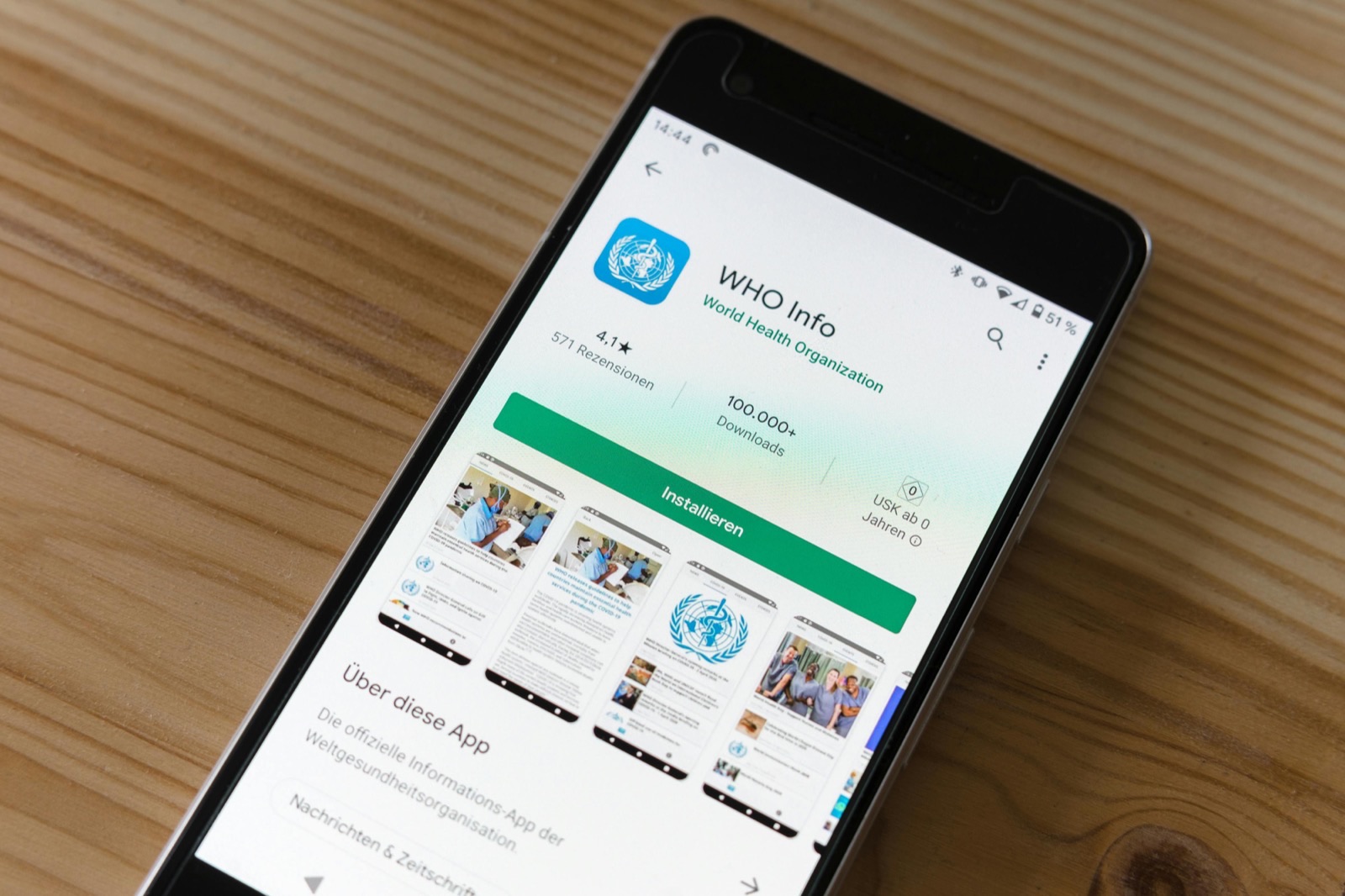 Black smartphone displaying WHO Info app page with blue WHO logo, 4.1 star rating, 571 reviews, 100,000+ downloads, green Install button, and preview