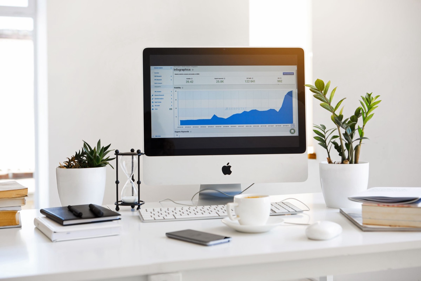 A desktop computer on a white desk showing an SEO analytics dashboard with a rising visibility graph