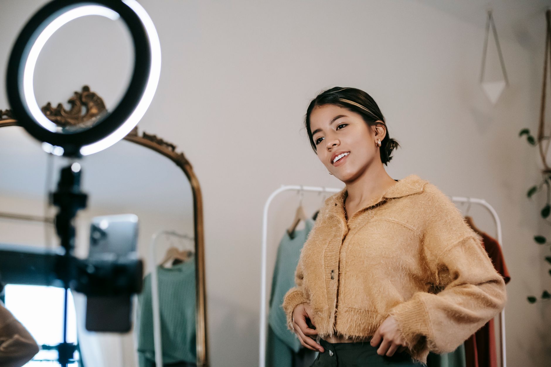 Woman in beige cardigan smiling while sitting in front of a ring light during what appears to be a content creation session