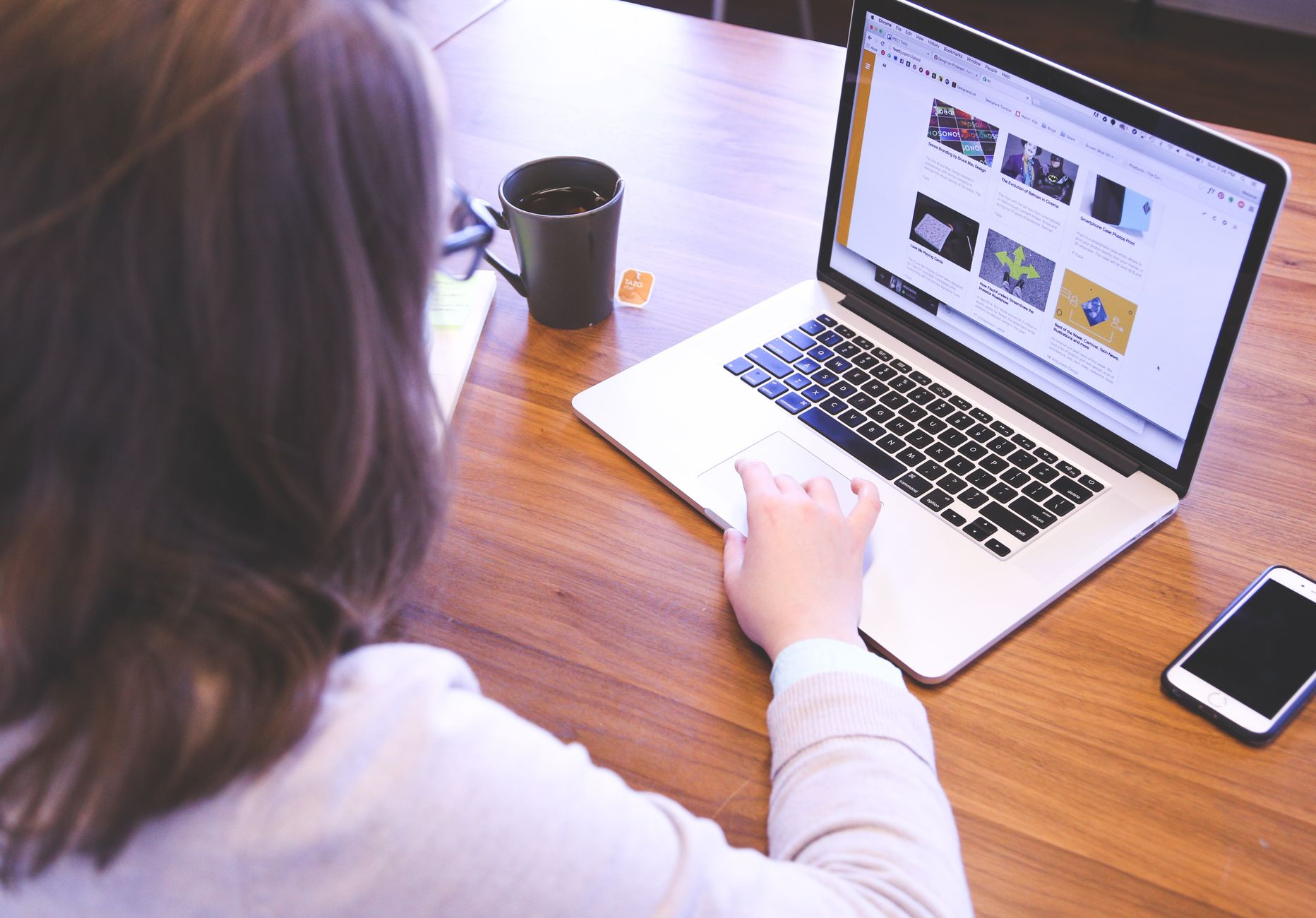 Person working at wooden desk with laptop displaying website, coffee mug, and smartphone nearby