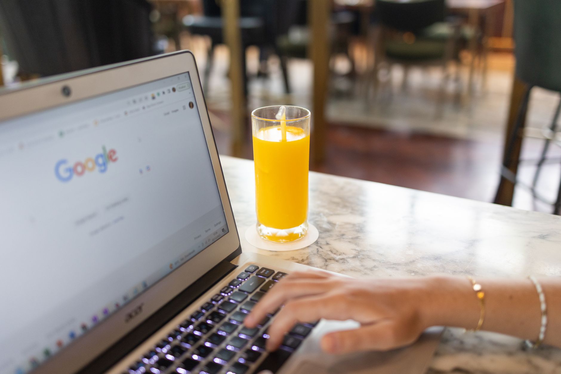 Person typing on laptop displaying Google homepage with glass of orange juice on marble table