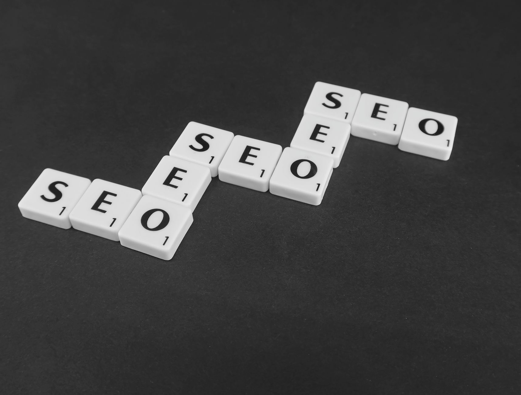 Three sets of Scrabble tiles spelling SEO arranged in ascending steps on a dark background