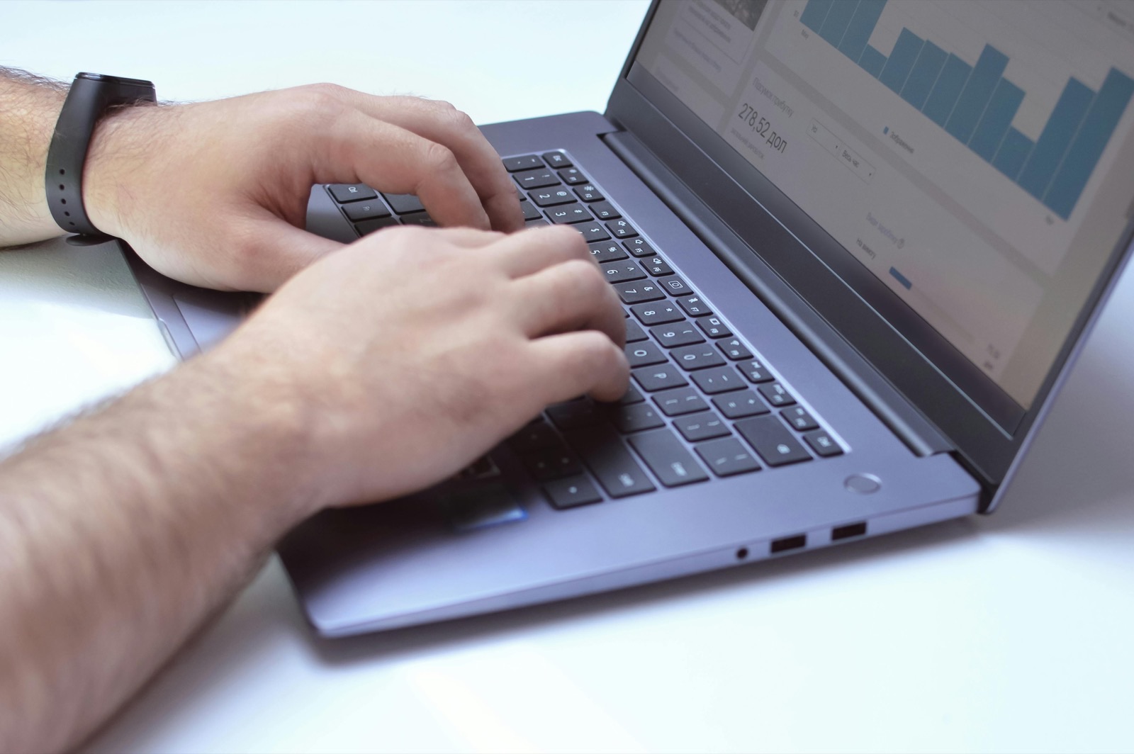 Person typing on a laptop keyboard with a bar chart displayed on the screen