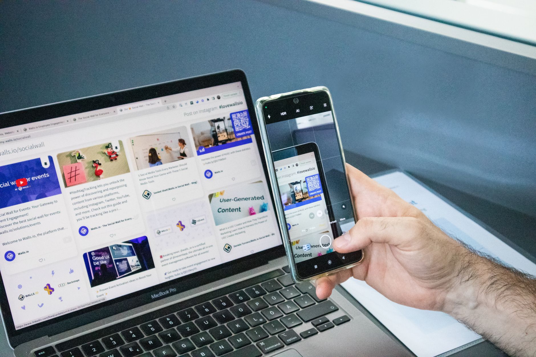 Person holding smartphone displaying website content next to MacBook Pro laptop showing same website on larger screen