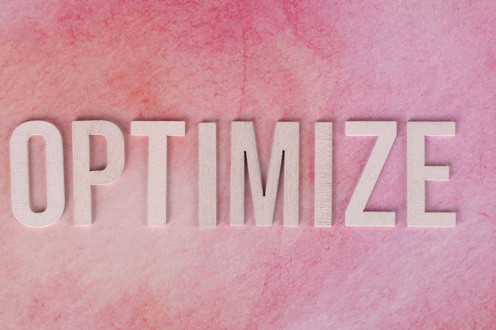 White wooden letters spelling "OPTIMIZE" on a pink textured background