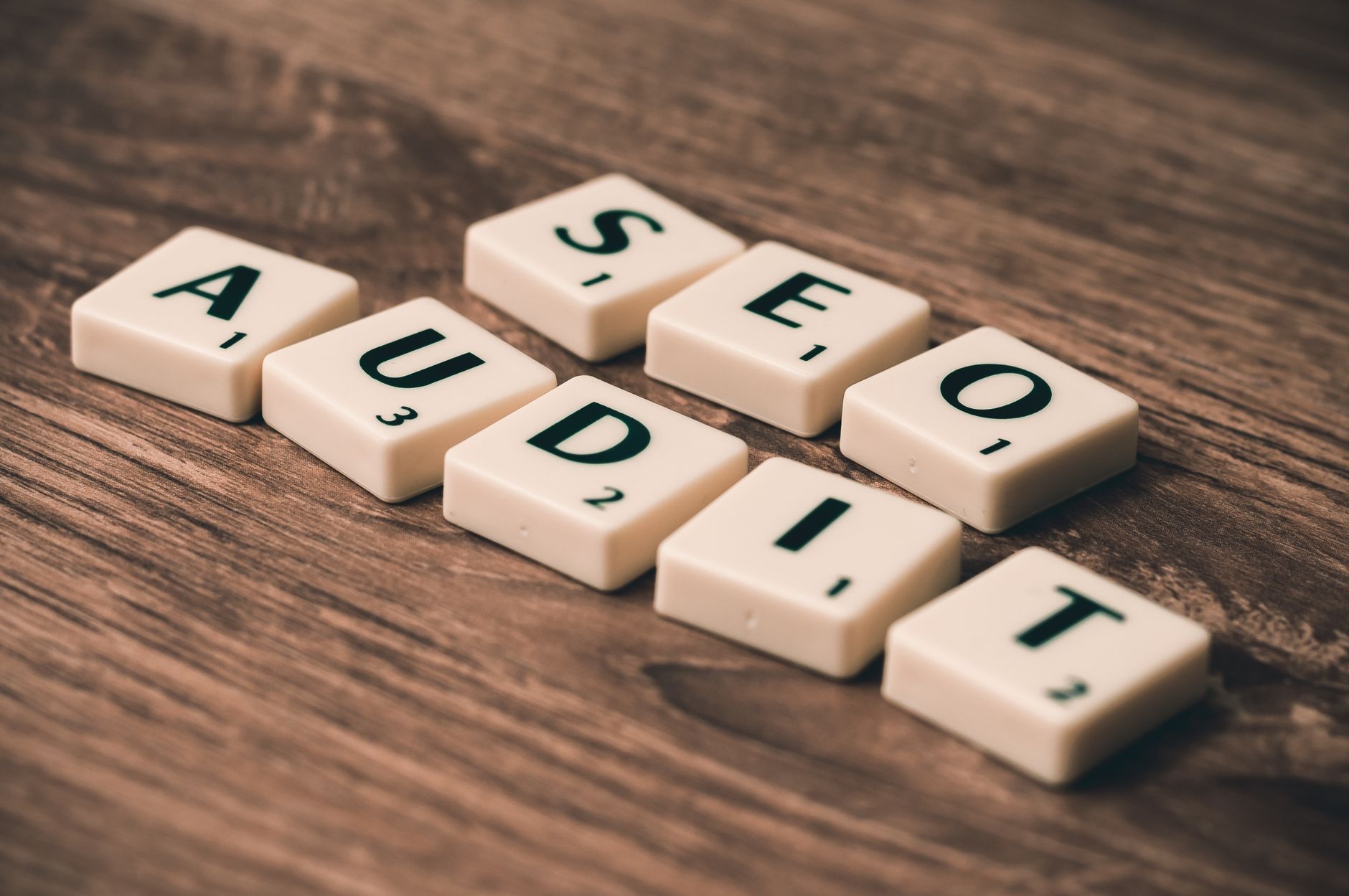 Scrabble tiles spelling "AUDIT" arranged on a wooden surface
