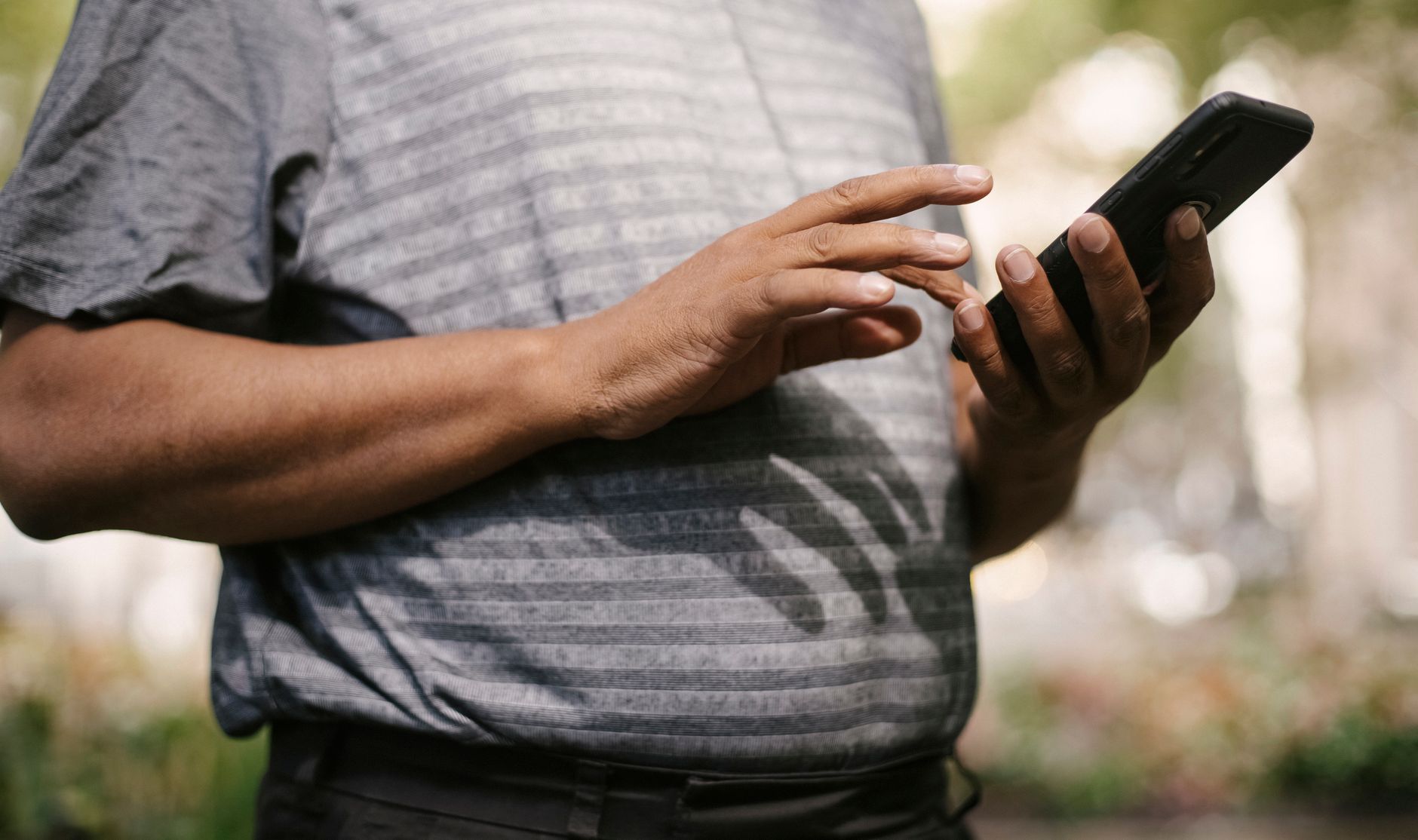 Person wearing gray striped shirt holding and looking at a black smartphone outdoors