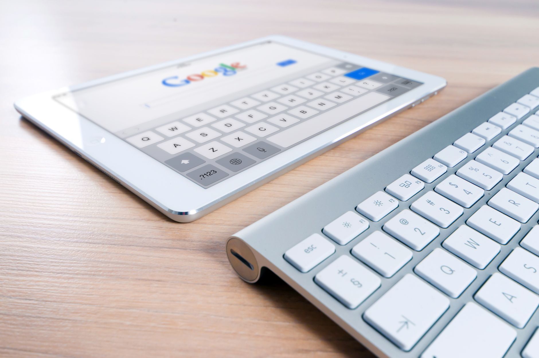 White tablet displaying Google search interface with keyboard visible on wooden desk