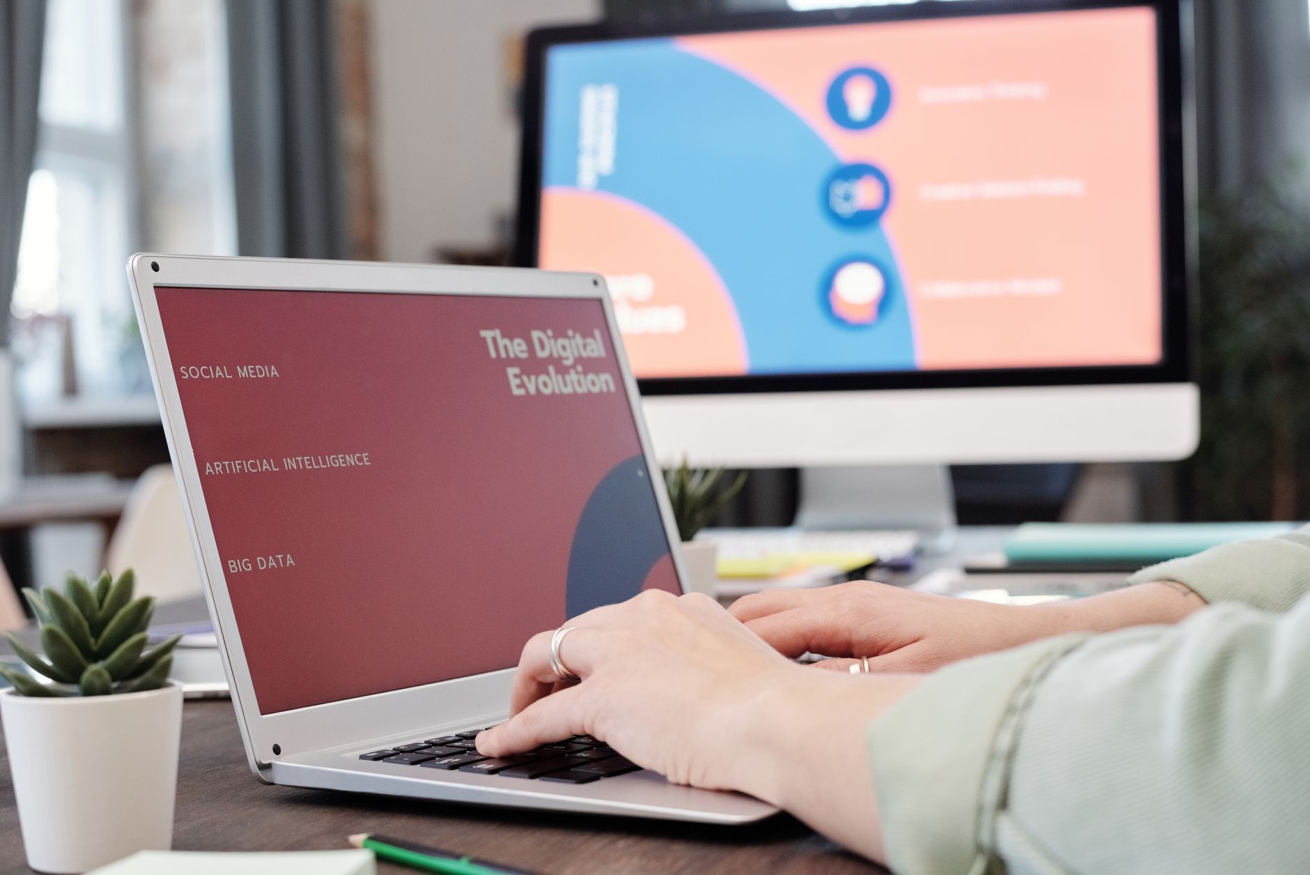 Person working on laptop displaying digital evolution presentation with monitor in background showing related content