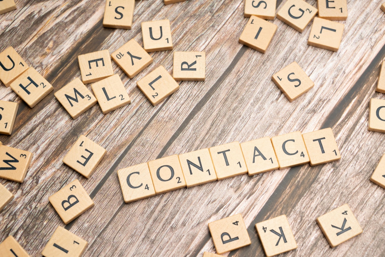 Scrabble tiles scattered on a wooden surface spelling out the word CONTACT