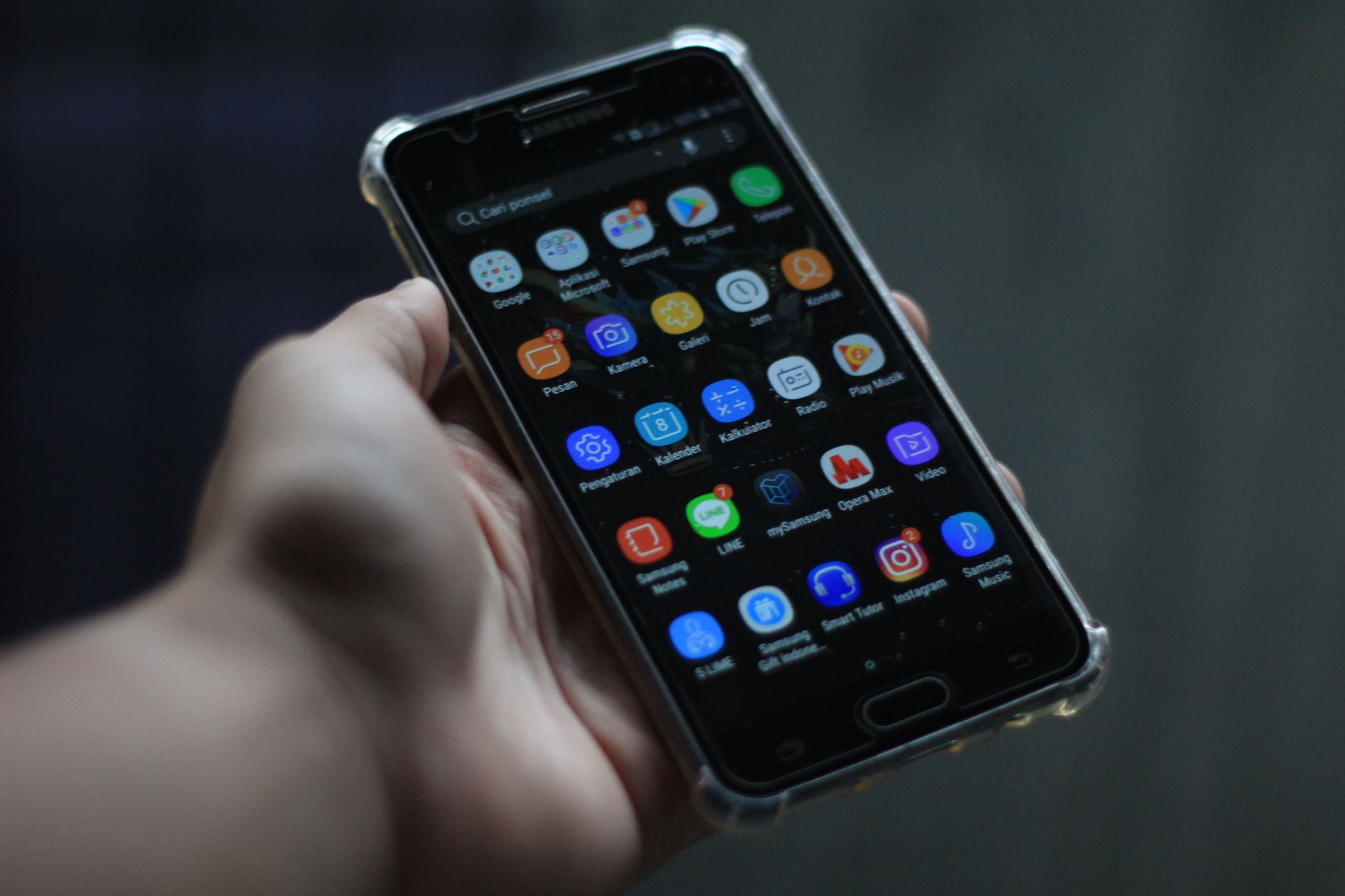 Hand holding a smartphone with a dark theme display showing multiple colorful app icons arranged in a grid layout
