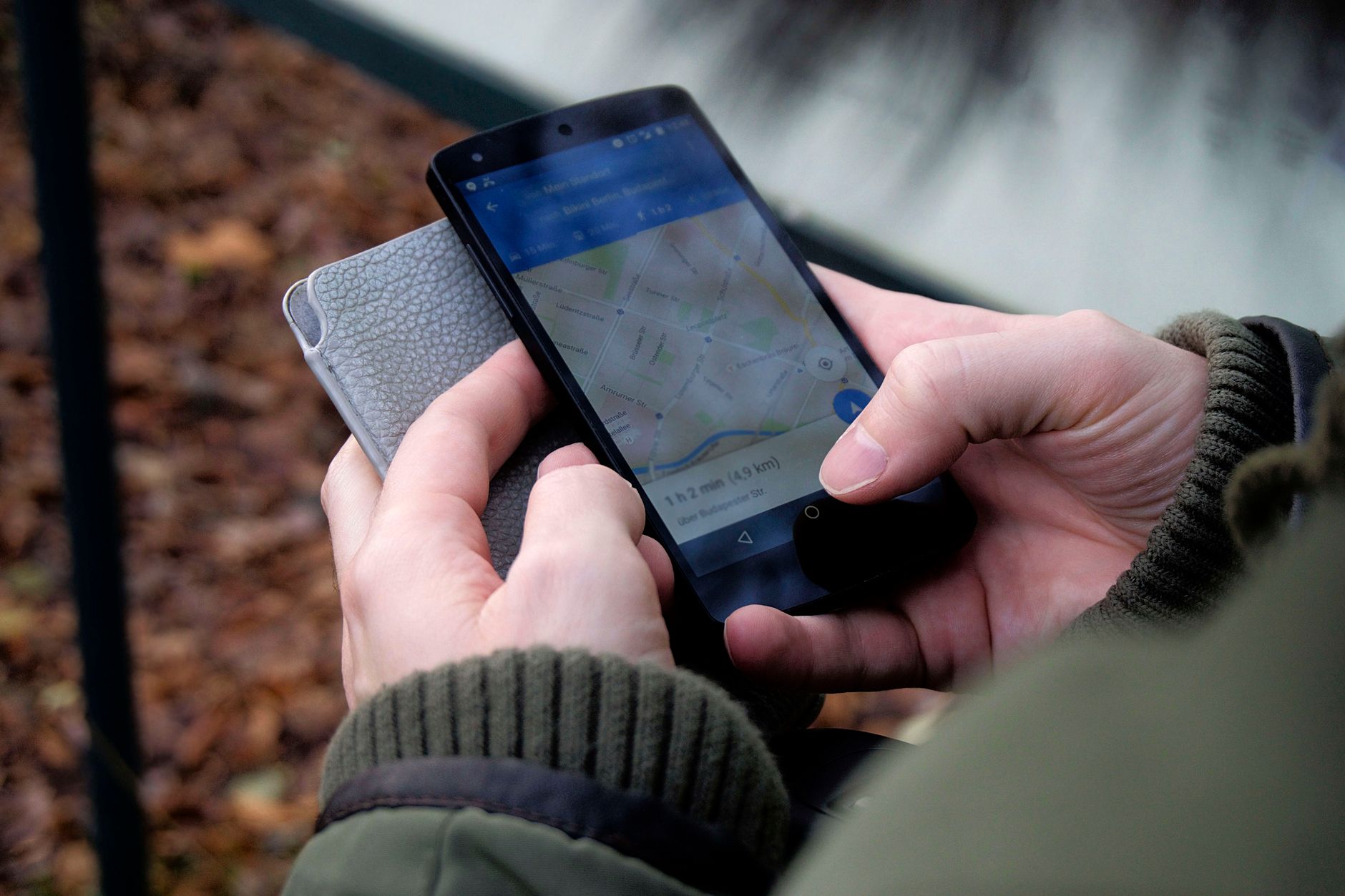 Person holding a smartphone displaying a map application with blue interface and route information outdoors near a brick wall