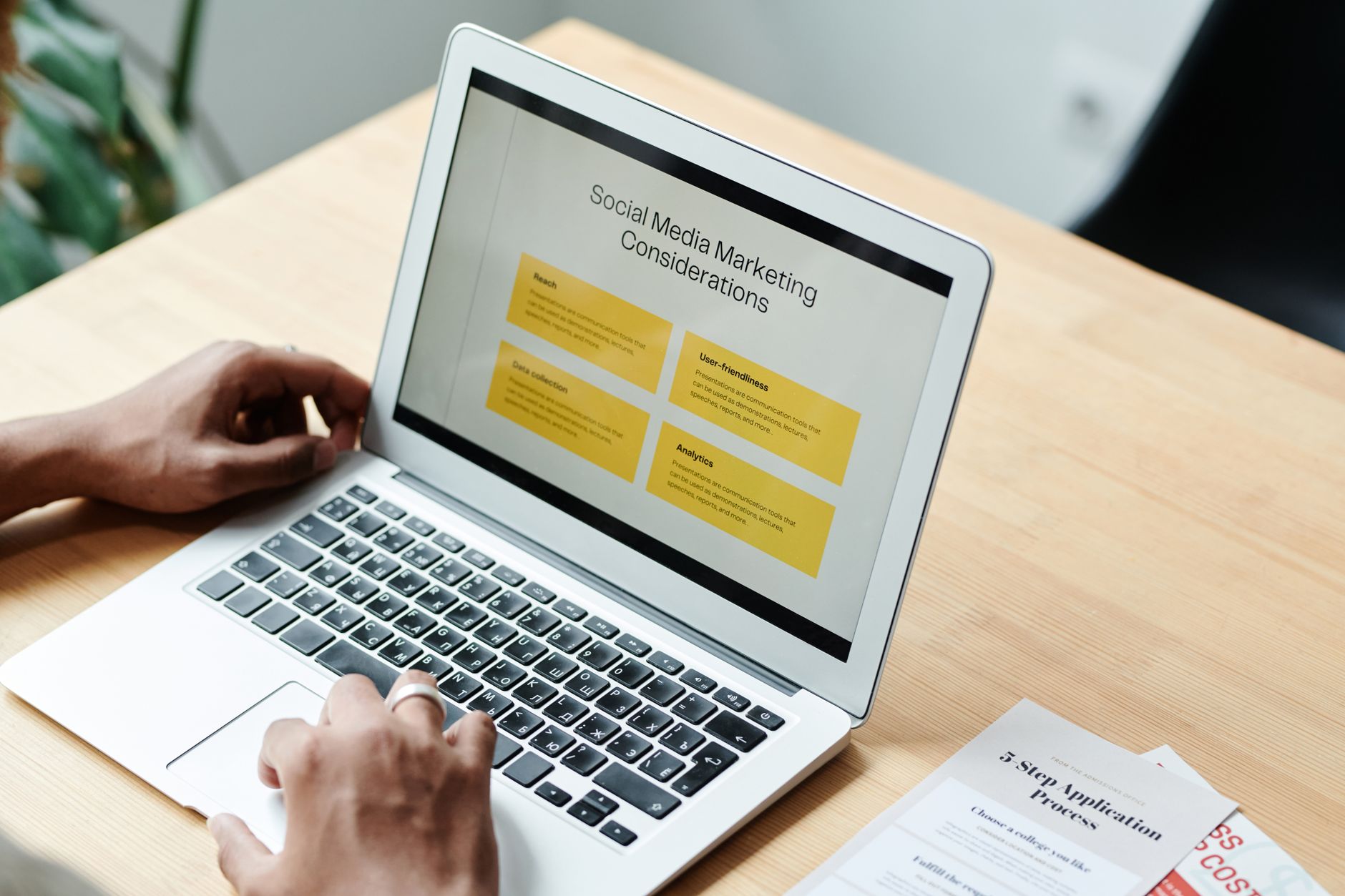 Person working on laptop displaying Social Media Marketing Considerations with yellow highlighted boxes on wooden desk