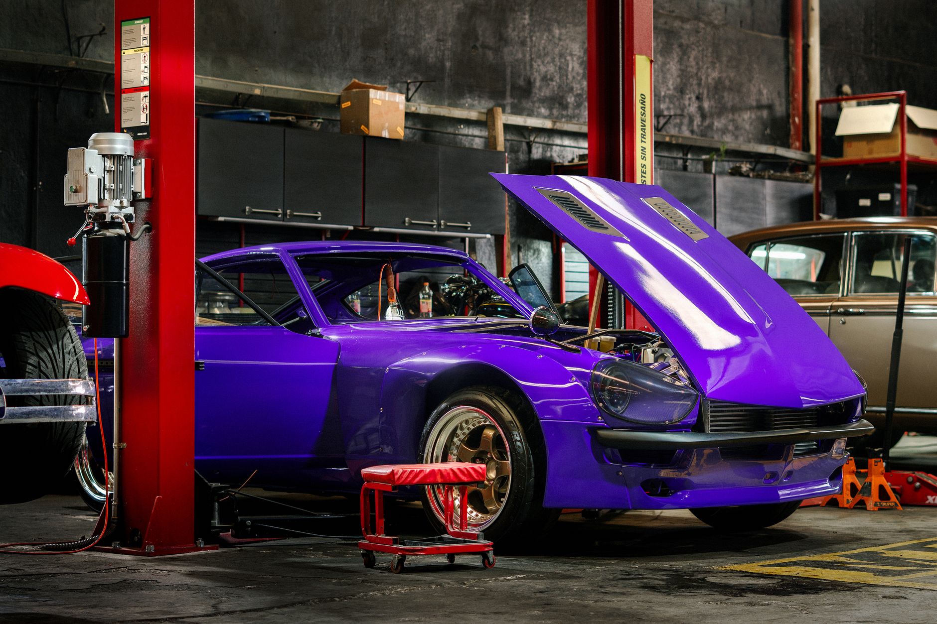 A car raised on a shop lift with the hood open in a repair bay