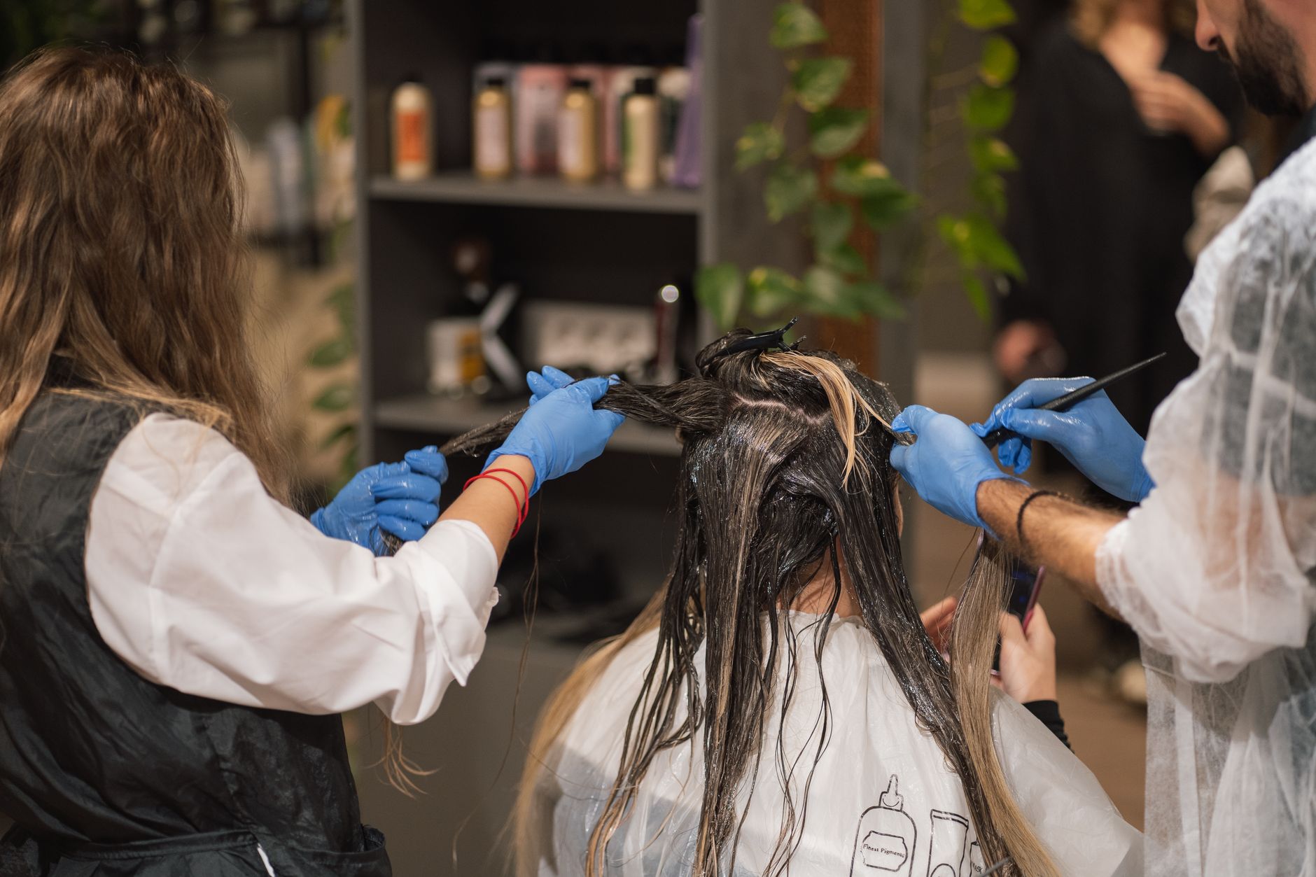 Two stylists applying color to a client's hair in a salon