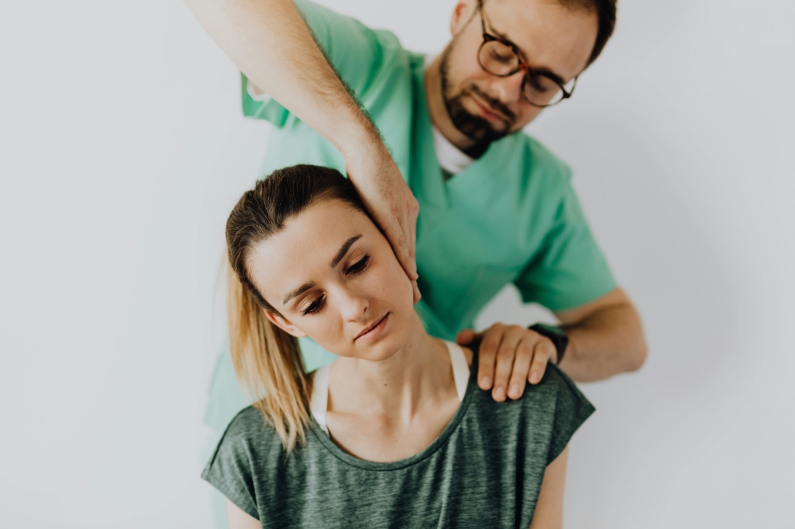 A physical therapist guiding a seated patient through a gentle neck and shoulder mobilization