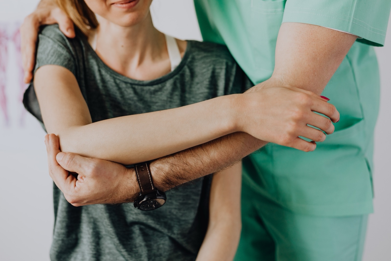 A therapist supporting a patient's arm across the chest during a guided shoulder range-of-motion exercise