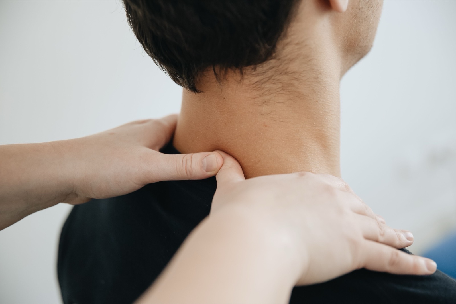 A therapist performing hands-on soft tissue work across a patient's shoulders and upper back