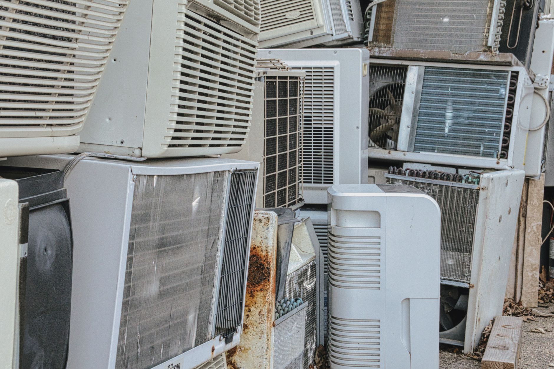 A stack of old rusted air conditioning units discarded outside a building