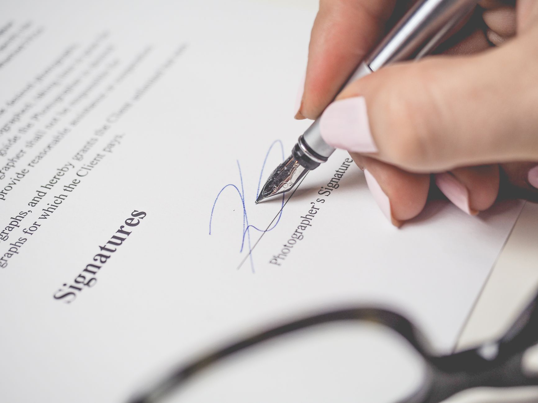 A hand signing the signature line of a legal document with a fountain pen