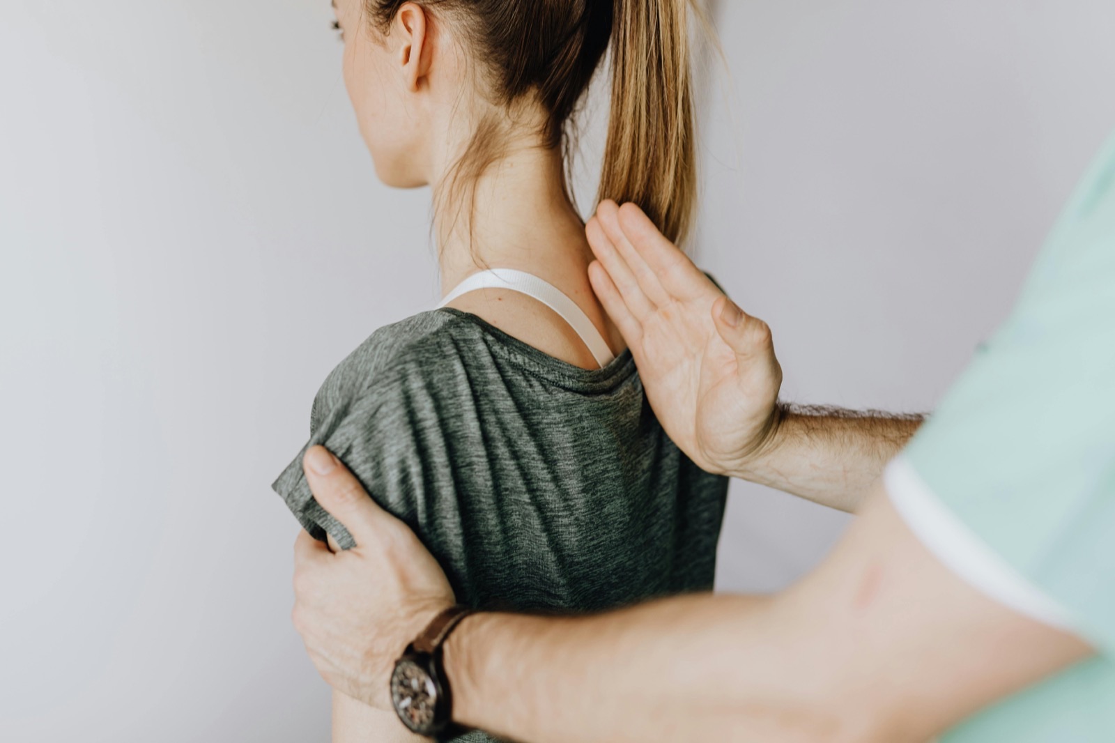A chiropractor assessing the alignment of a standing patient's upper back and shoulder