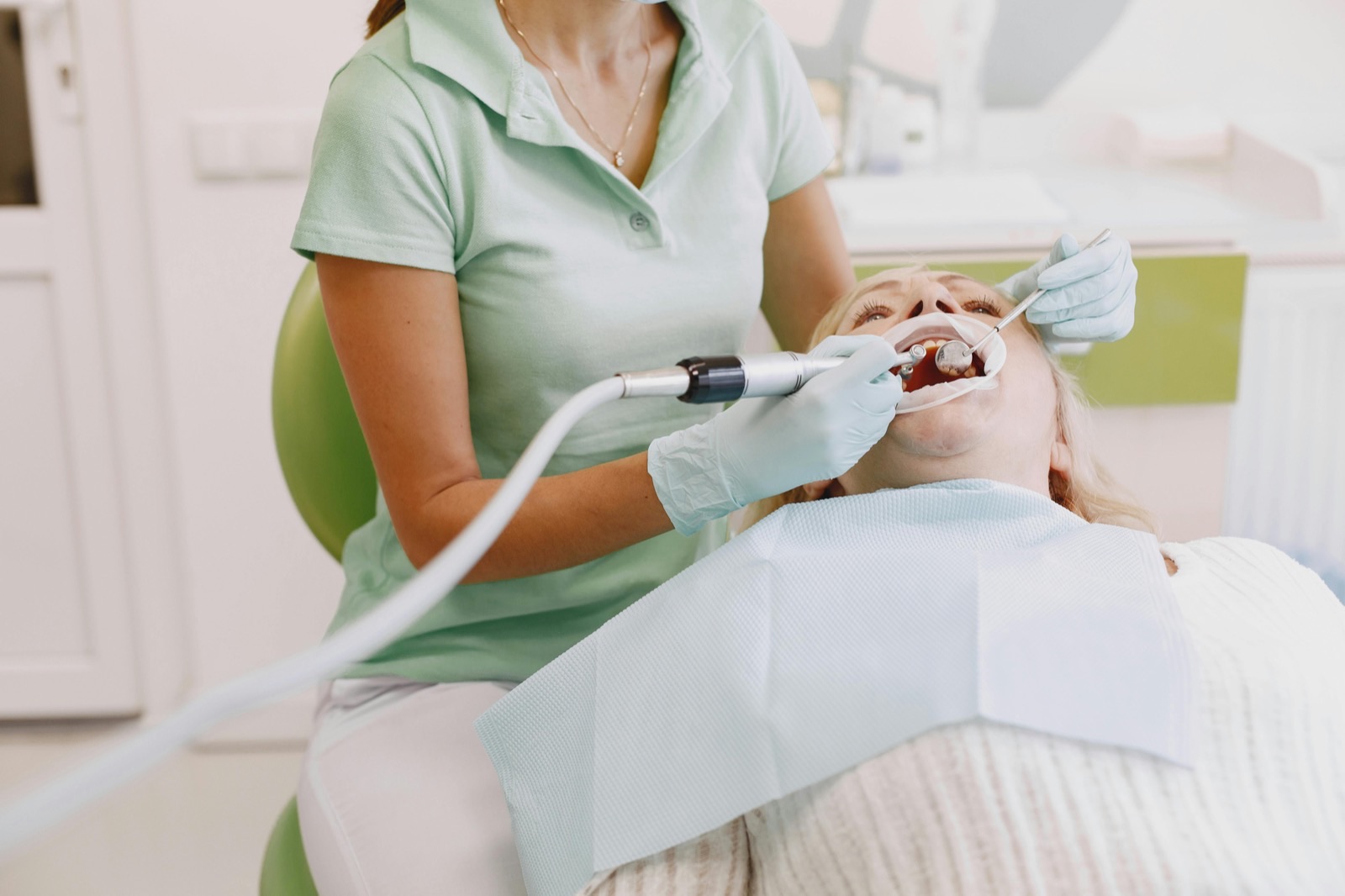 A dentist examining a reclined patient with a handpiece during a routine visit