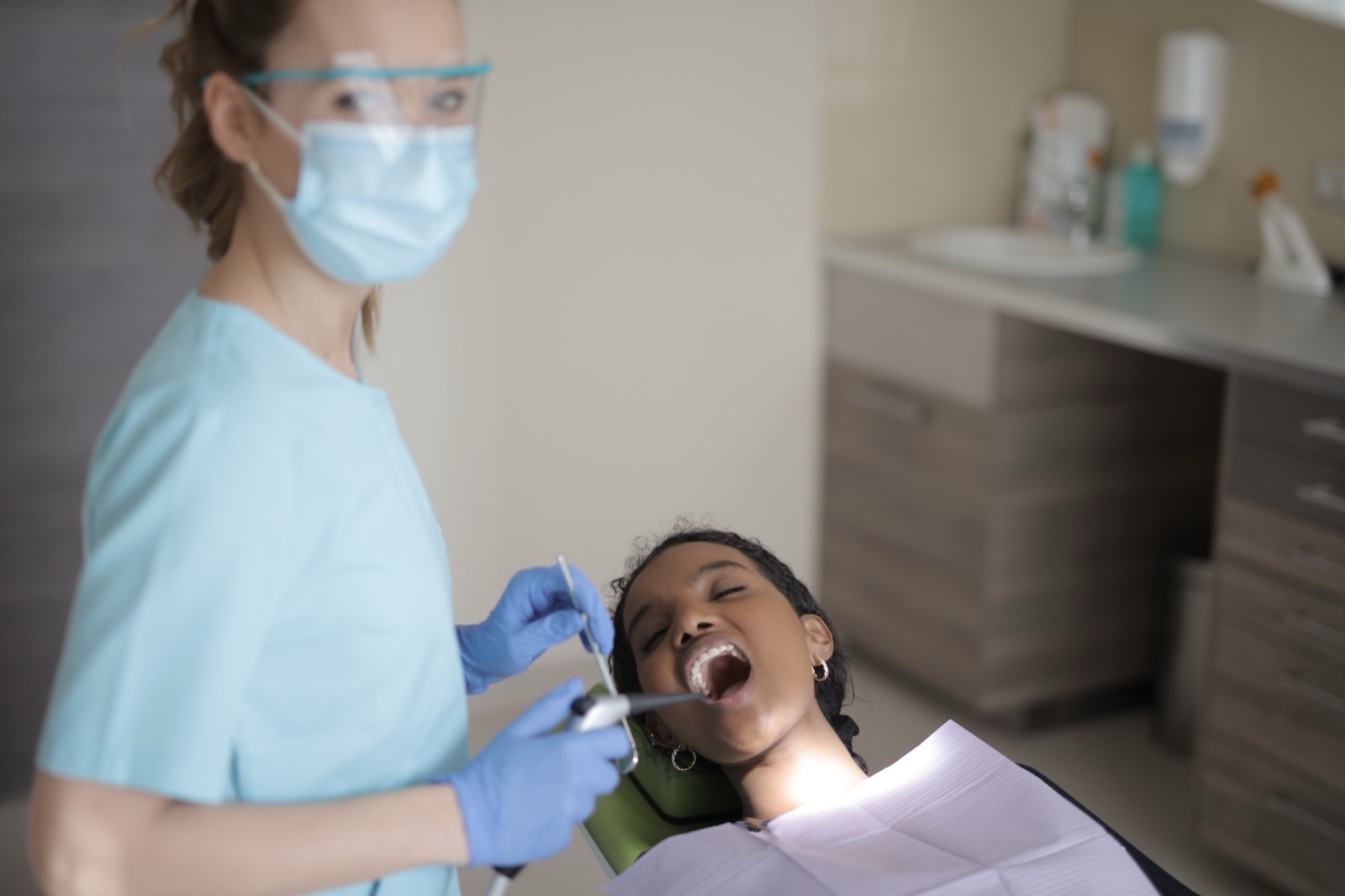 A dental hygienist in a mask and face shield preparing to examine a patient in the chair